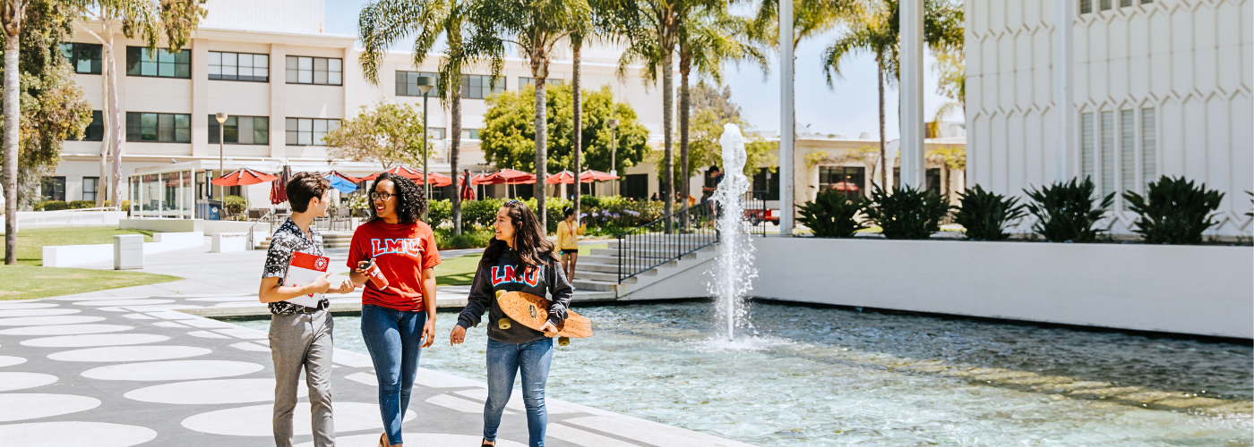 Three students walking next to Foley Pond together holding their class notebooks and a longboard.
